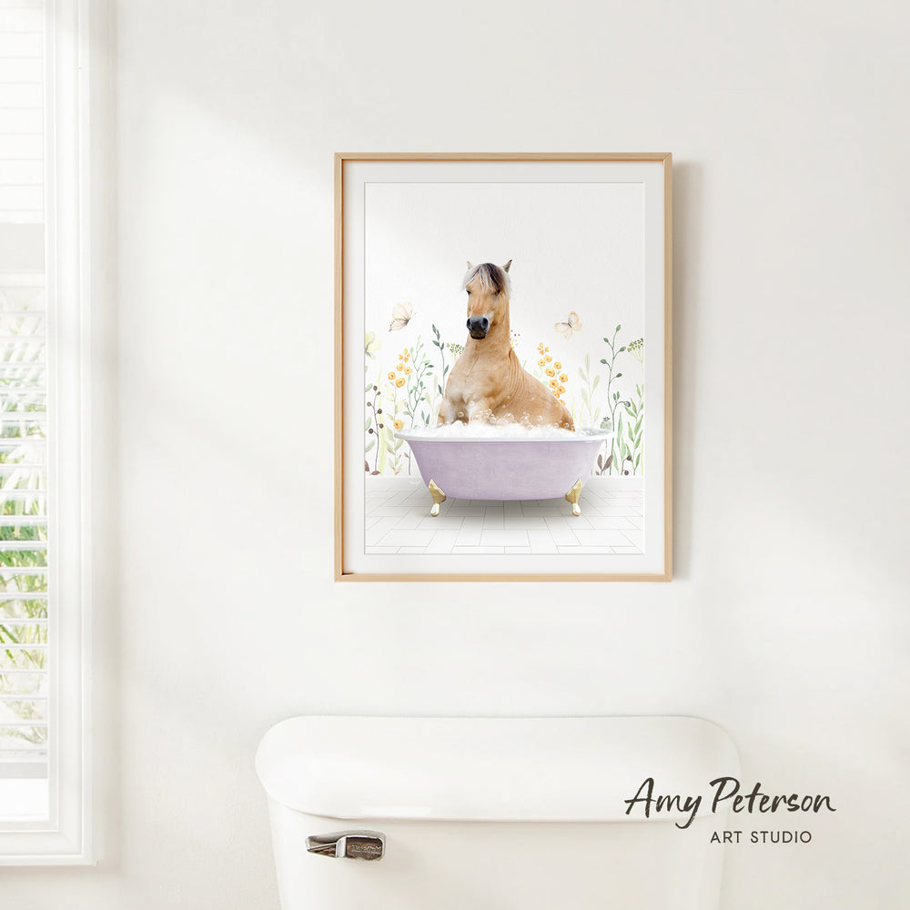 A framed image of a horse sitting in a bathtub, surrounded by flowers and butterflies, is hanging on a white wall.