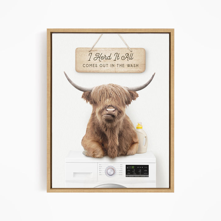 A framed image depicting a Highland cow sitting on a washing machine, with a sign above it that reads "I Herd It All Comes out in the Wash".