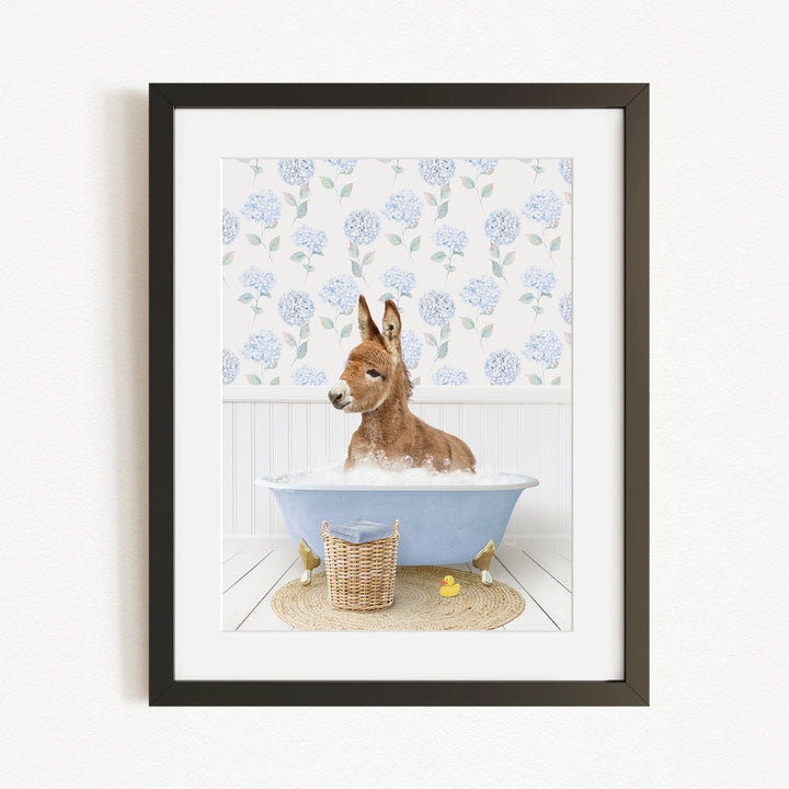 A donkey is sitting in a blue bathtub filled with water, surrounded by a floral patterned wall and a basket of rubber ducks.