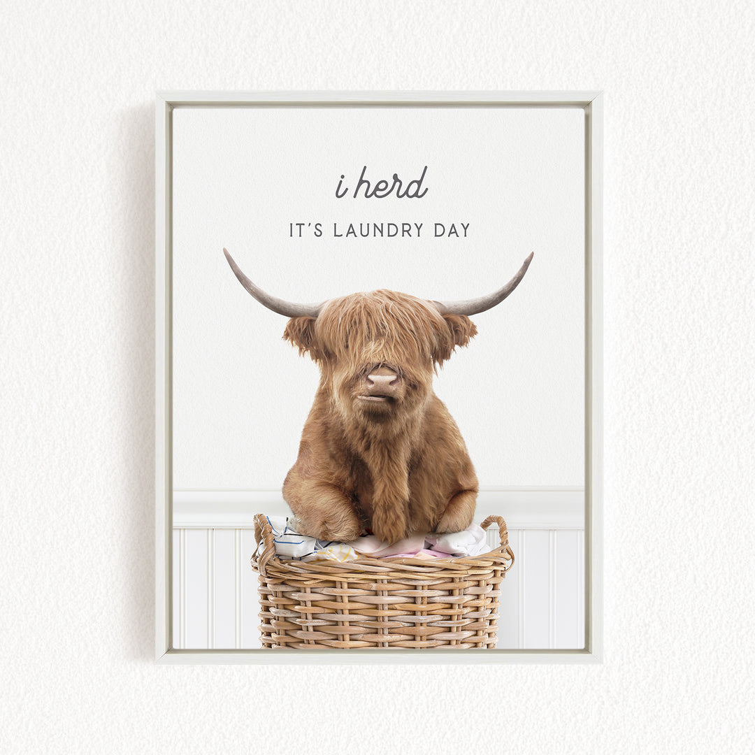 A brown cow with long horns is sitting in a wicker basket, with the text "i herd, it's laundry day" displayed above the image.
