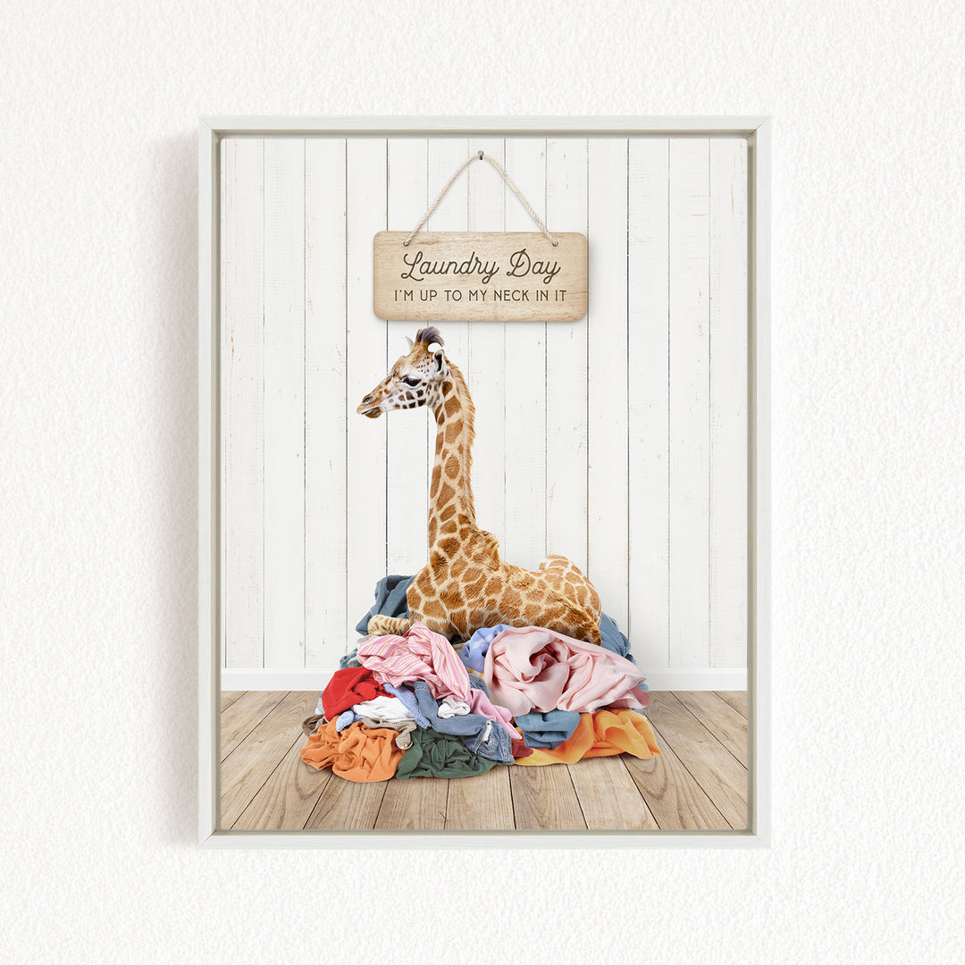 A giraffe sitting on a pile of clothes in front of a wooden sign that says "Laundry Day"