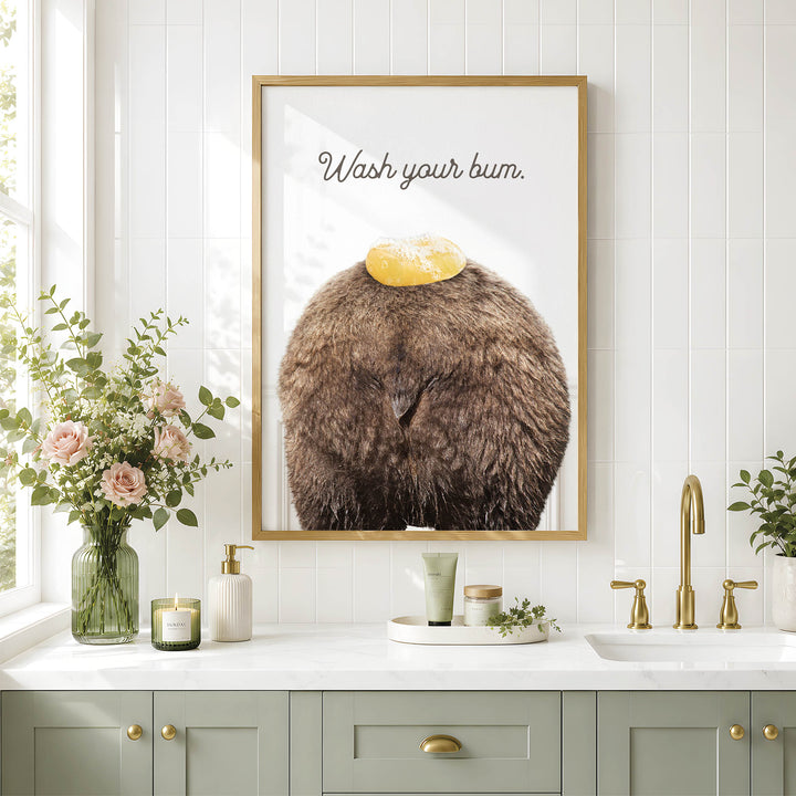 a bathroom counter with a framed poster of a bear's head with a yellow object on it, a vase of flowers, and various bathroom accessories such as a soap dispenser and a candle.