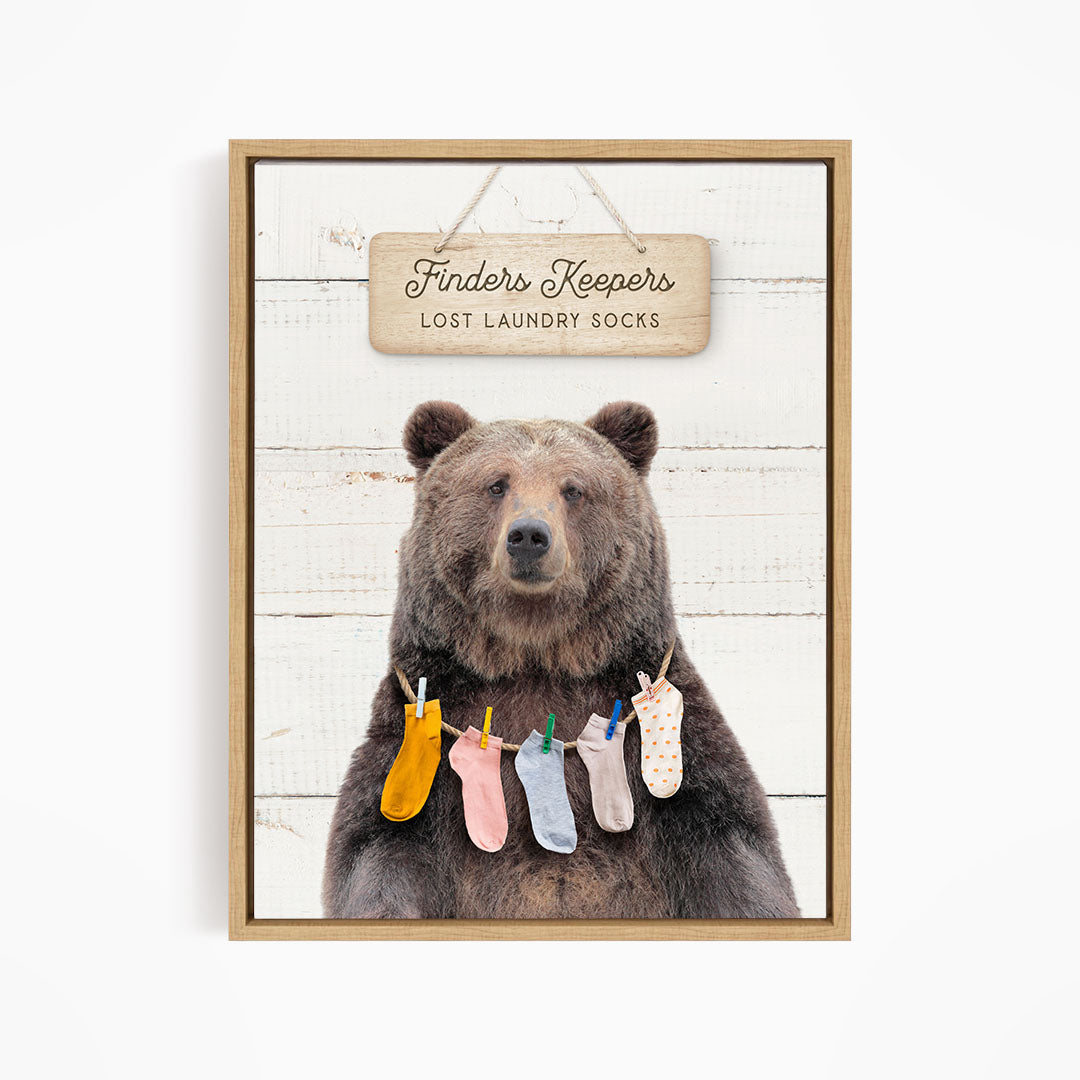 A wooden sign with the text "Finders Keepers" hangs above a bear wearing a colorful array of socks.