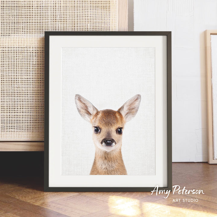 A framed print of a deer's face is displayed on a wooden floor, with a woven basket visible in the background.