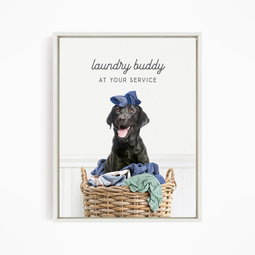 A black dog wearing a blue hat sits in a wicker laundry basket filled with clothes.