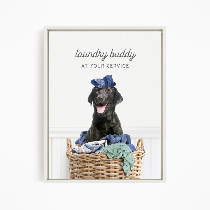 A black dog wearing a blue hat sits in a wicker laundry basket filled with clothes.