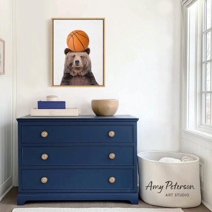 a blue dresser with a framed picture of a bear holding a basketball on its head, placed above it. The dresser has three drawers and a white basket next to it.