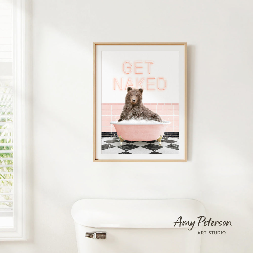 A framed print of a bear sitting in a pink bathtub with the text "GET NAKED" on it, hanging on a white wall.