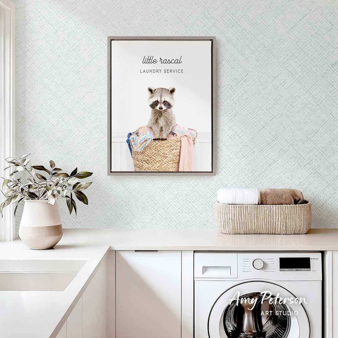 a laundry room with a framed photo of a raccoon sitting in a basket, a potted plant, and a basket of towels on a counter.