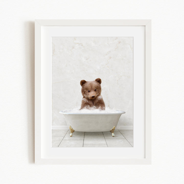 A cute brown bear sitting in a white bathtub filled with bubbles, looking directly at the camera.