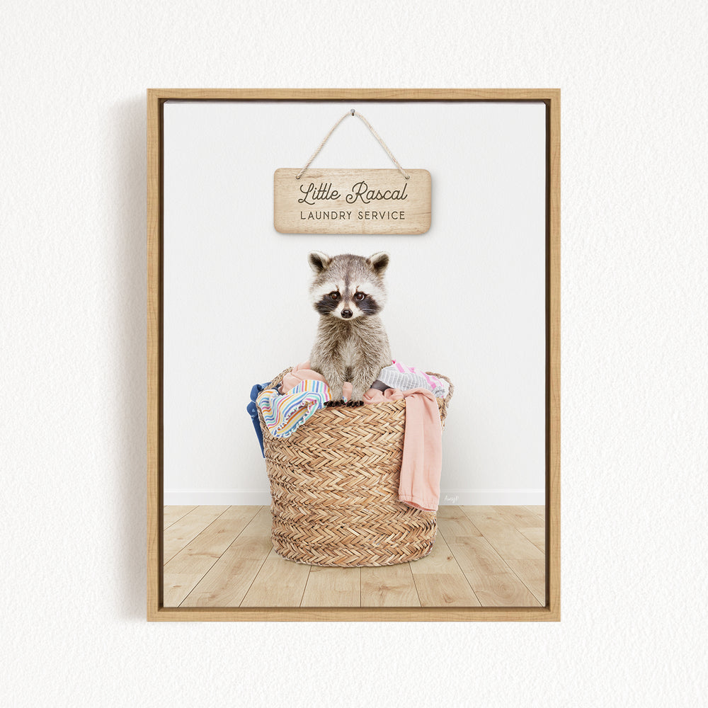 A raccoon sitting in a woven laundry basket, with a sign for "Little Racal Laundry Service" hanging above it.