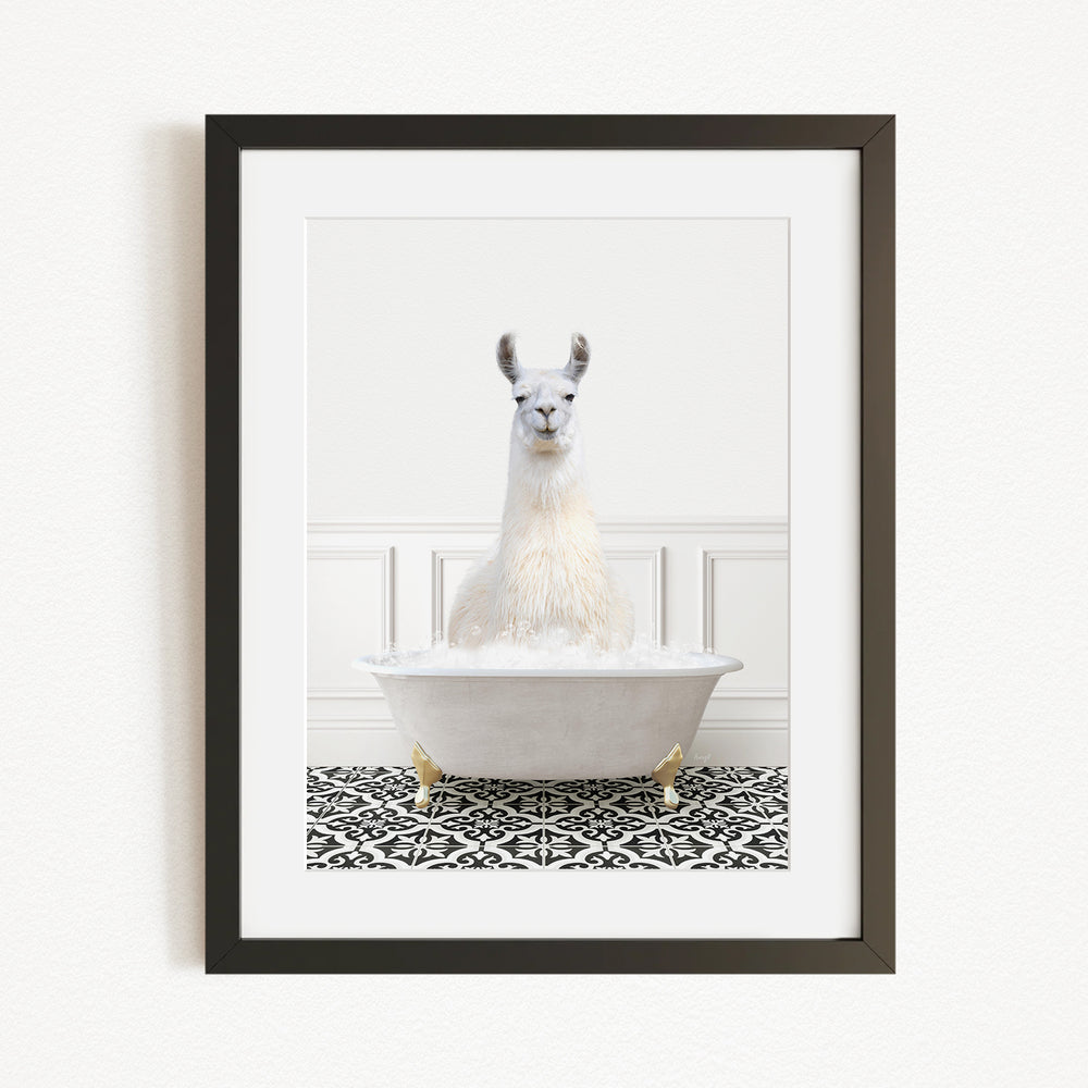 A white llama sitting in a white bathtub filled with bubbles, with a black and white patterned rug on the floor in front of the tub.