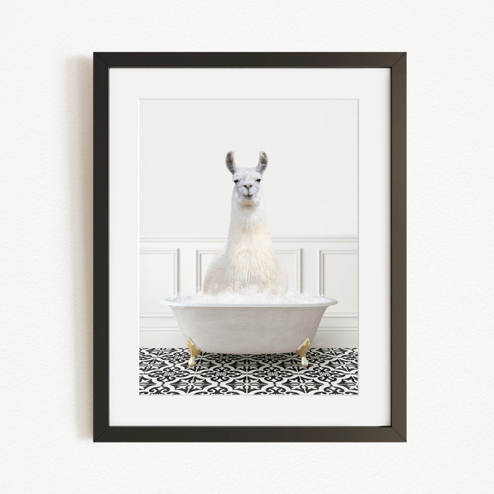 A white llama sitting in a white bathtub filled with bubbles, with a black and white patterned rug on the floor in front of the tub.
