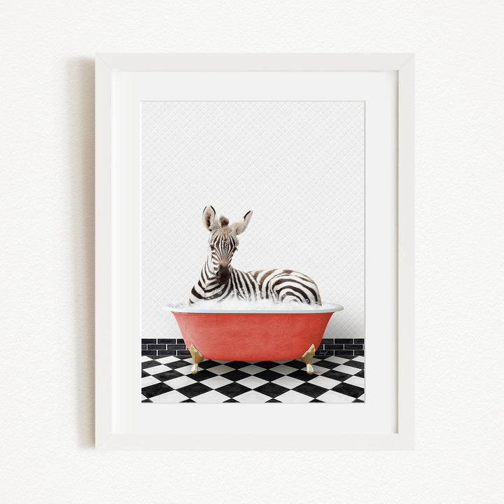 A zebra is sitting in a red bathtub on a black and white checkered floor.