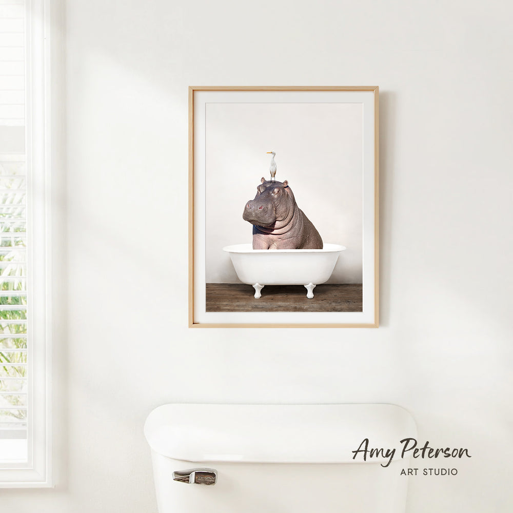 A framed photograph of a hippopotamus sitting in a bathtub, with a bird perched on its head.