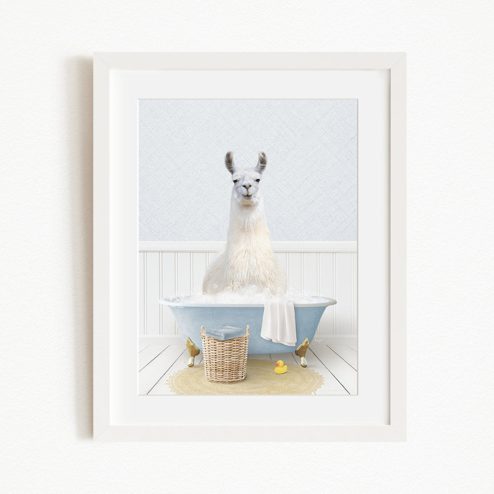 A white llama sitting in a blue bathtub filled with bubbles, surrounded by a yellow rubber duck and a woven basket.