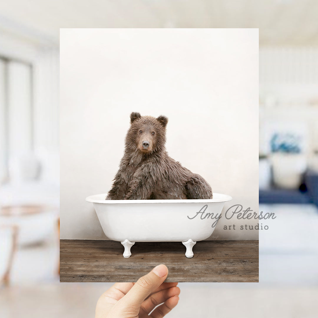 a hand holding up a polaroid picture of a bear in a bathtub