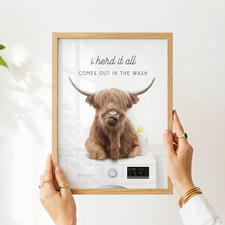 A person is holding up a framed image of a brown cow with horns, which appears to be a humorous or playful depiction of a washing machine.