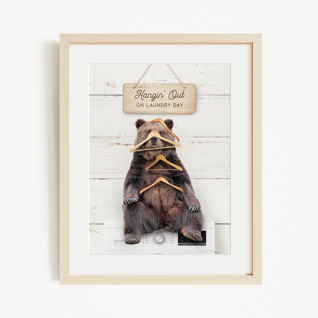 A framed image of a brown bear sitting on a washing machine, with a sign above it that says "Hangin' Out on laundry day".