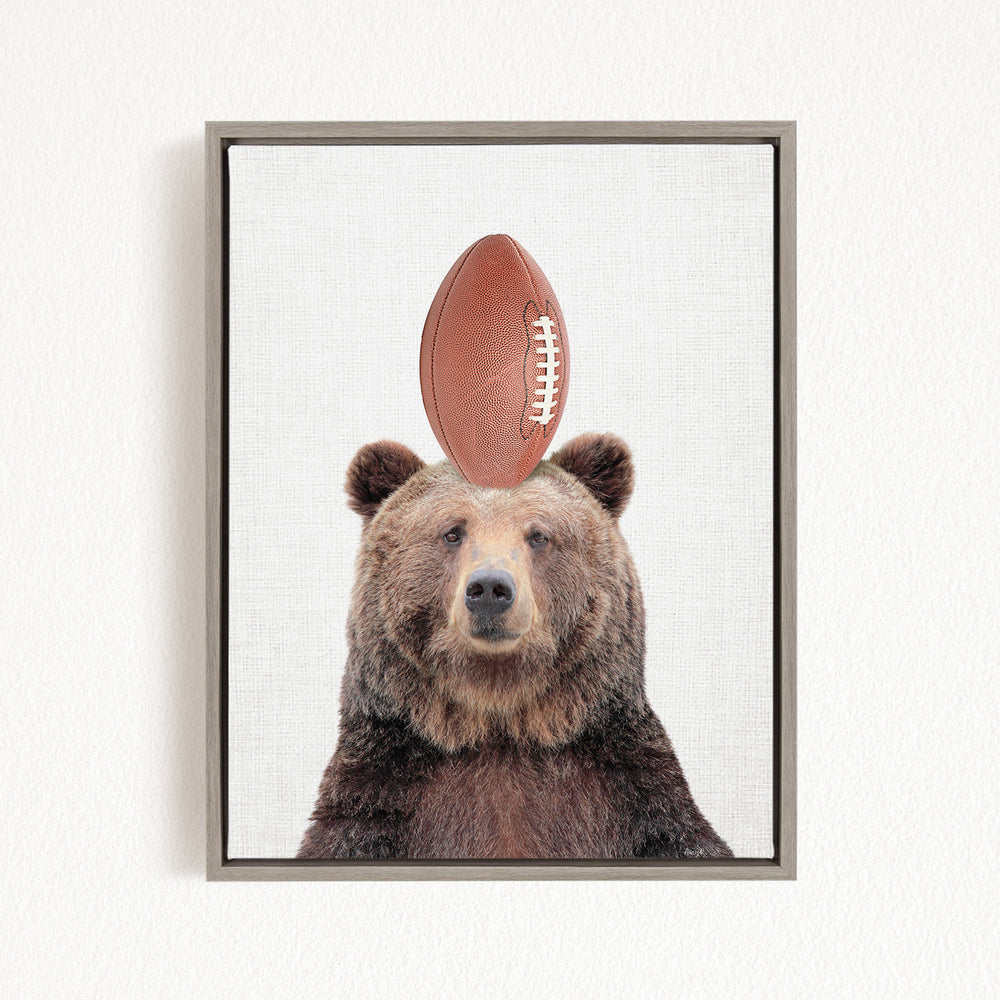 A brown bear standing on its head with a football on top of its head.