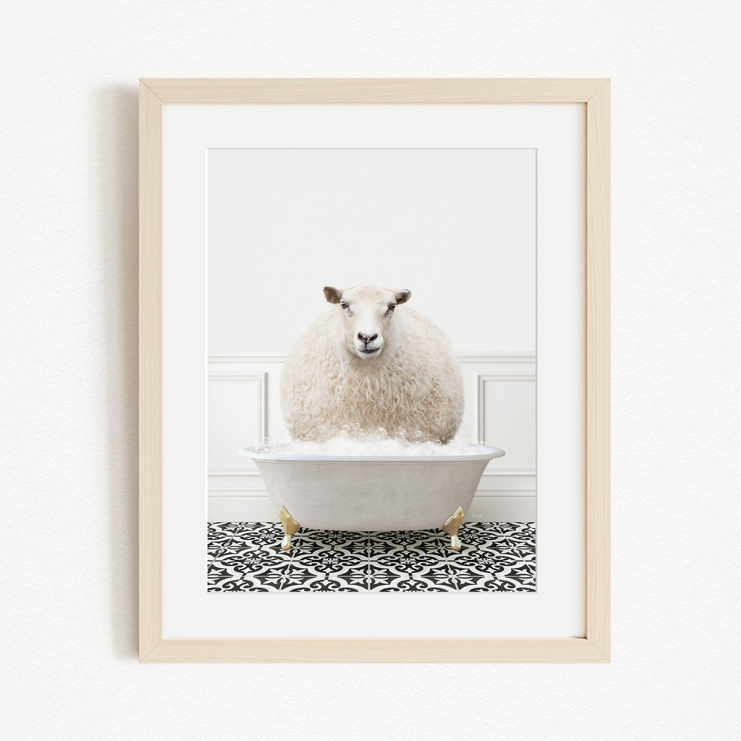 A fluffy white sheep sits in a white bathtub filled with bubbles, surrounded by a black and white patterned rug on the floor.