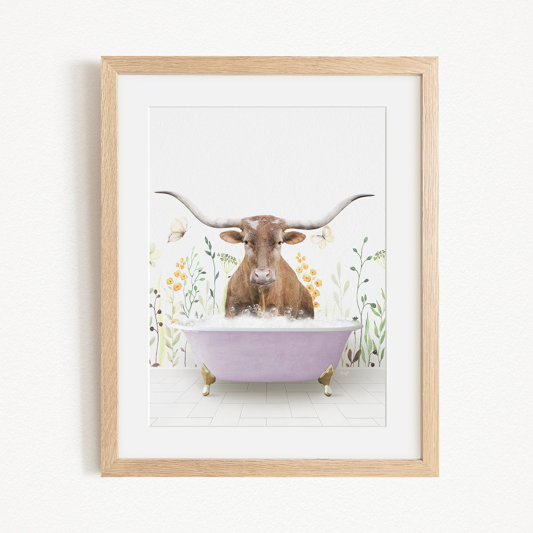 A framed print depicting a brown cow with large horns sitting in a purple bathtub, surrounded by flowers and butterflies.