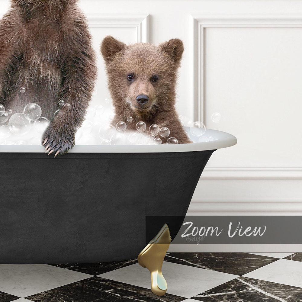 A young bear cub sitting in a bathtub filled with bubbles, with a black bathtub and a gold bathtub leg visible.