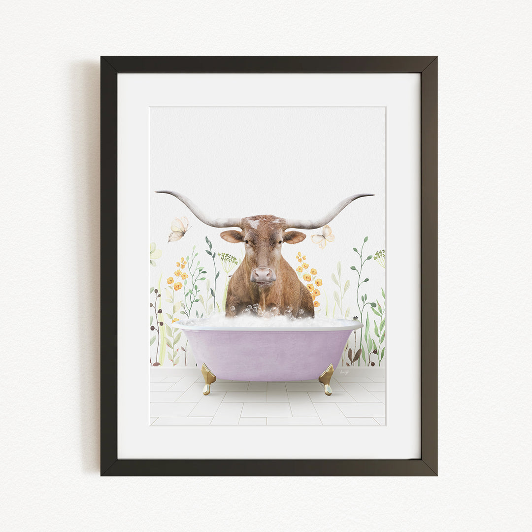 A framed print depicting a brown cow with large horns sitting in a purple bathtub, surrounded by flowers and plants.