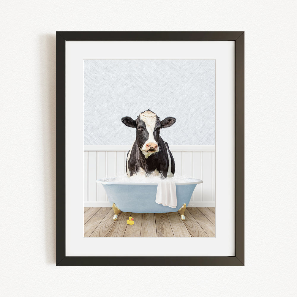 A black and white cow is sitting in a blue bathtub filled with water, with a towel draped over the side of the tub.