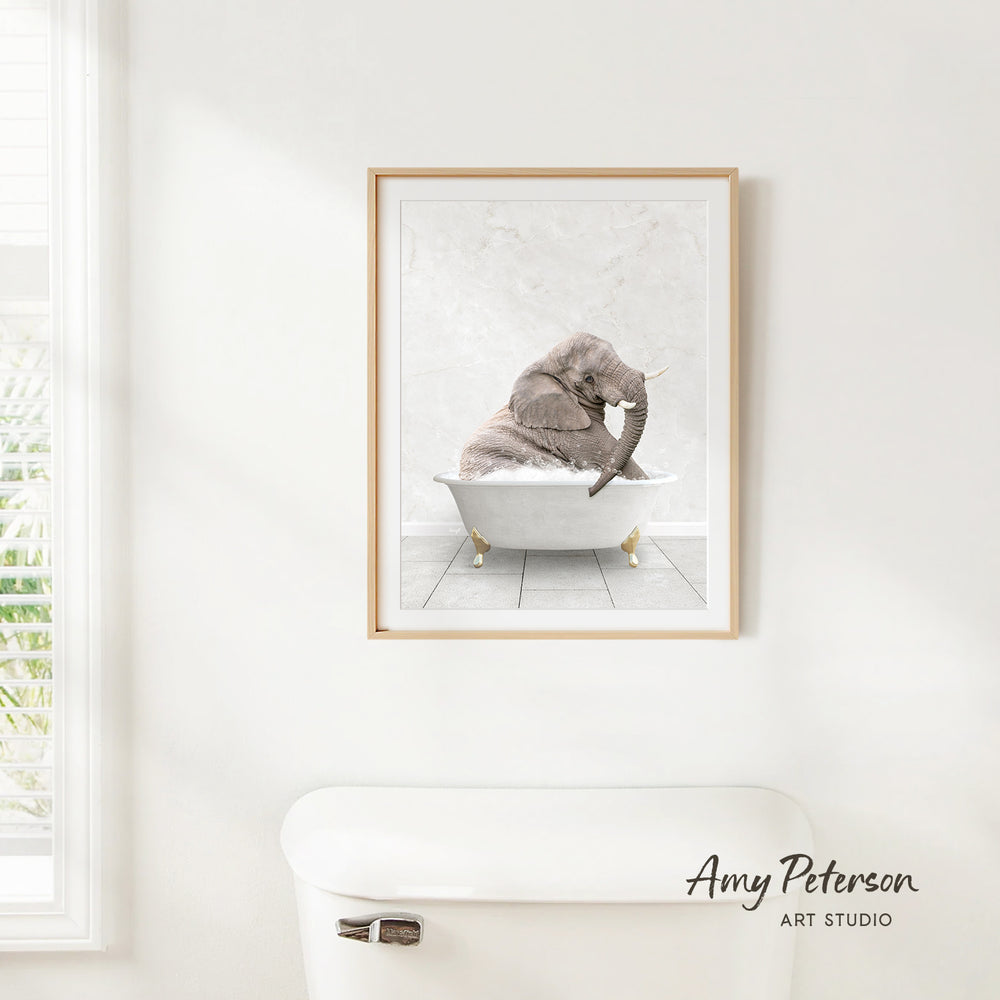 A framed image of an elephant sitting in a bathtub is hanging on a white wall.