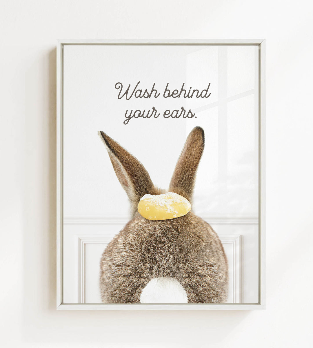 A framed image of a rabbit's ears with a yellow object on top, accompanied by the text "Wash behind your ears."