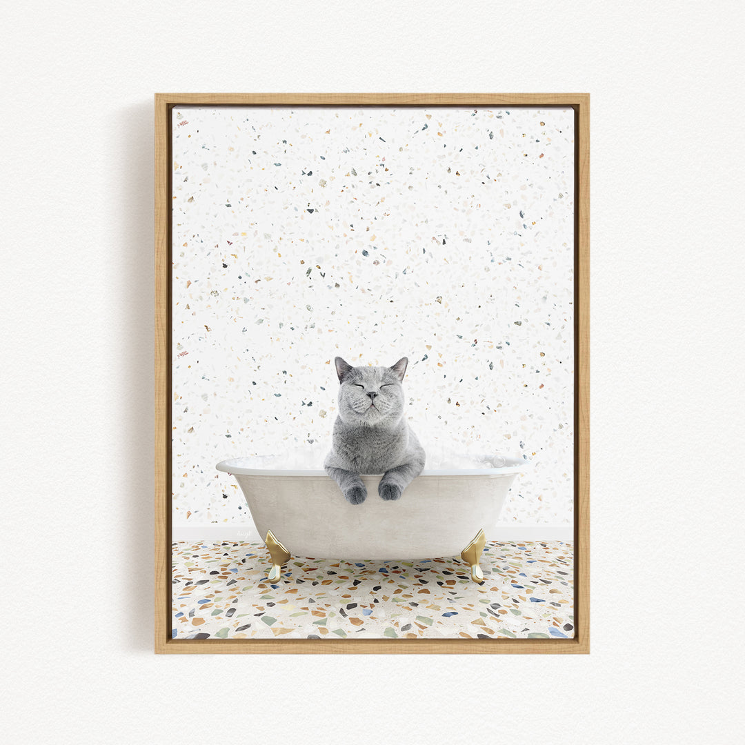 A gray cat sitting in a white bathtub filled with bubbles, surrounded by a speckled tiled floor.