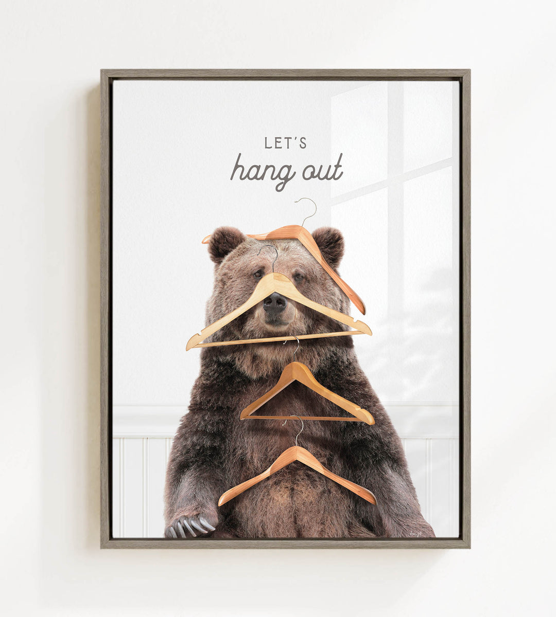 A framed image of a bear sitting on a shelf with multiple wooden hangers hanging from its head and shoulders, creating a humorous and whimsical scene.
