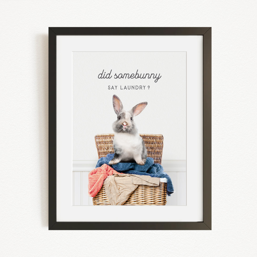 A gray and white rabbit sitting in a wicker basket filled with clothes, with the text "did some bunny say laundry?" displayed above the image.