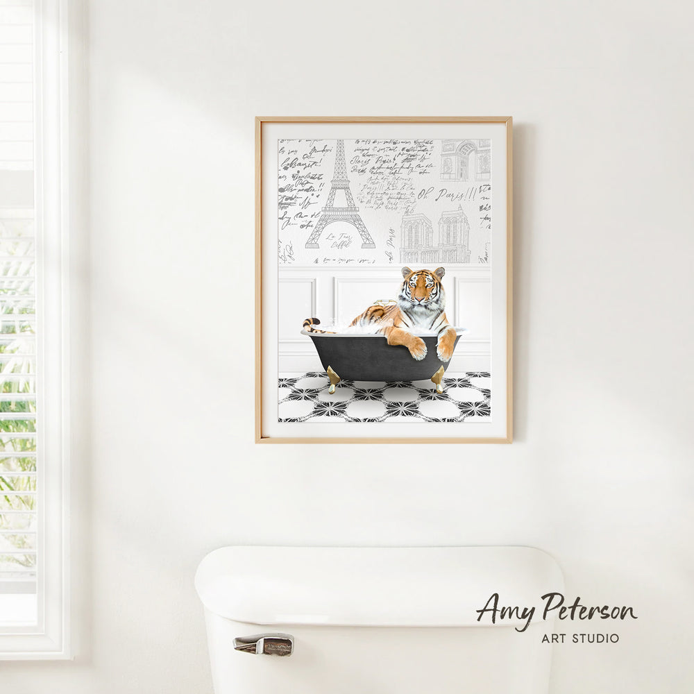 A framed print of a tiger sitting in a bathtub is hanging on a white wall, with a window and a toilet visible in the background.