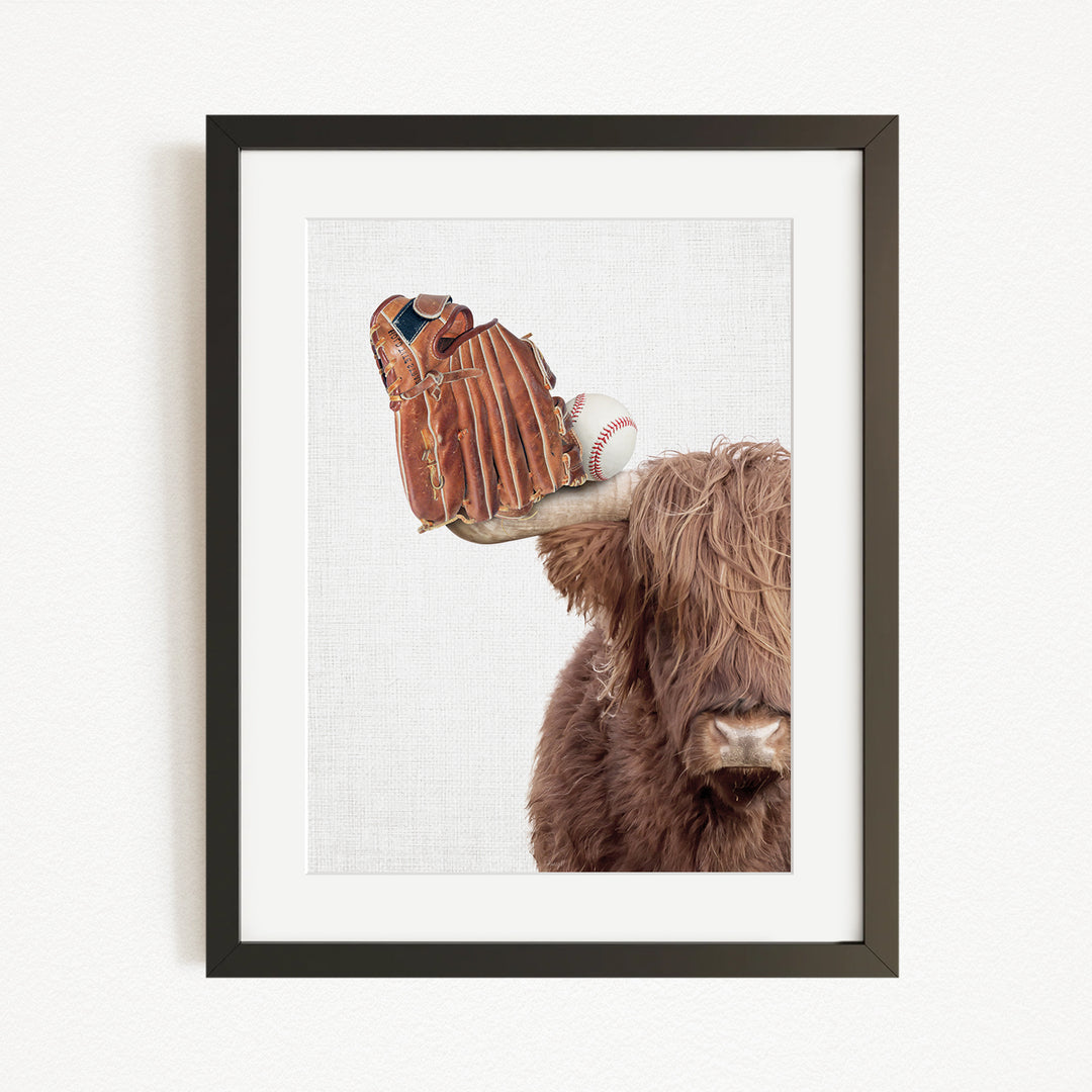 A framed image depicting a brown cow with a baseball glove on its head.