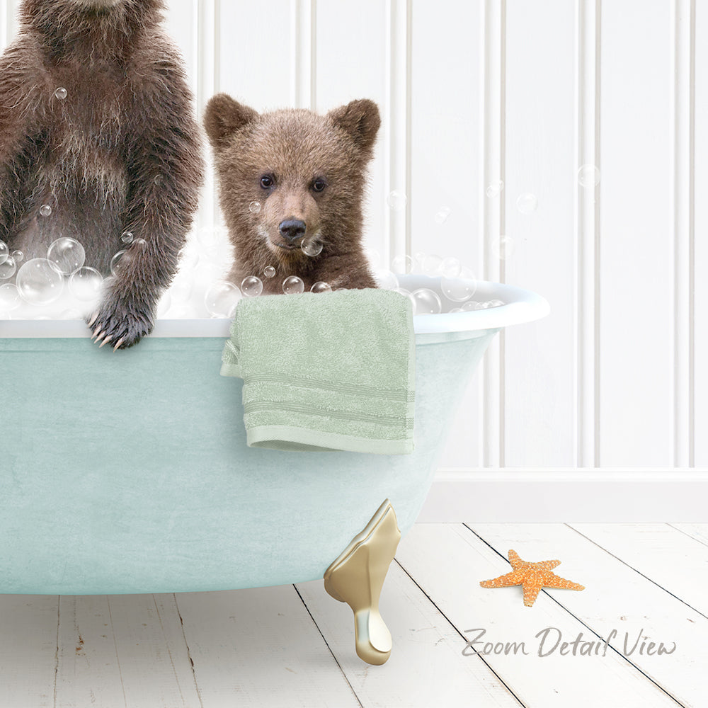 A baby bear sitting in a bathtub filled with bubbles, with a towel and starfish nearby.