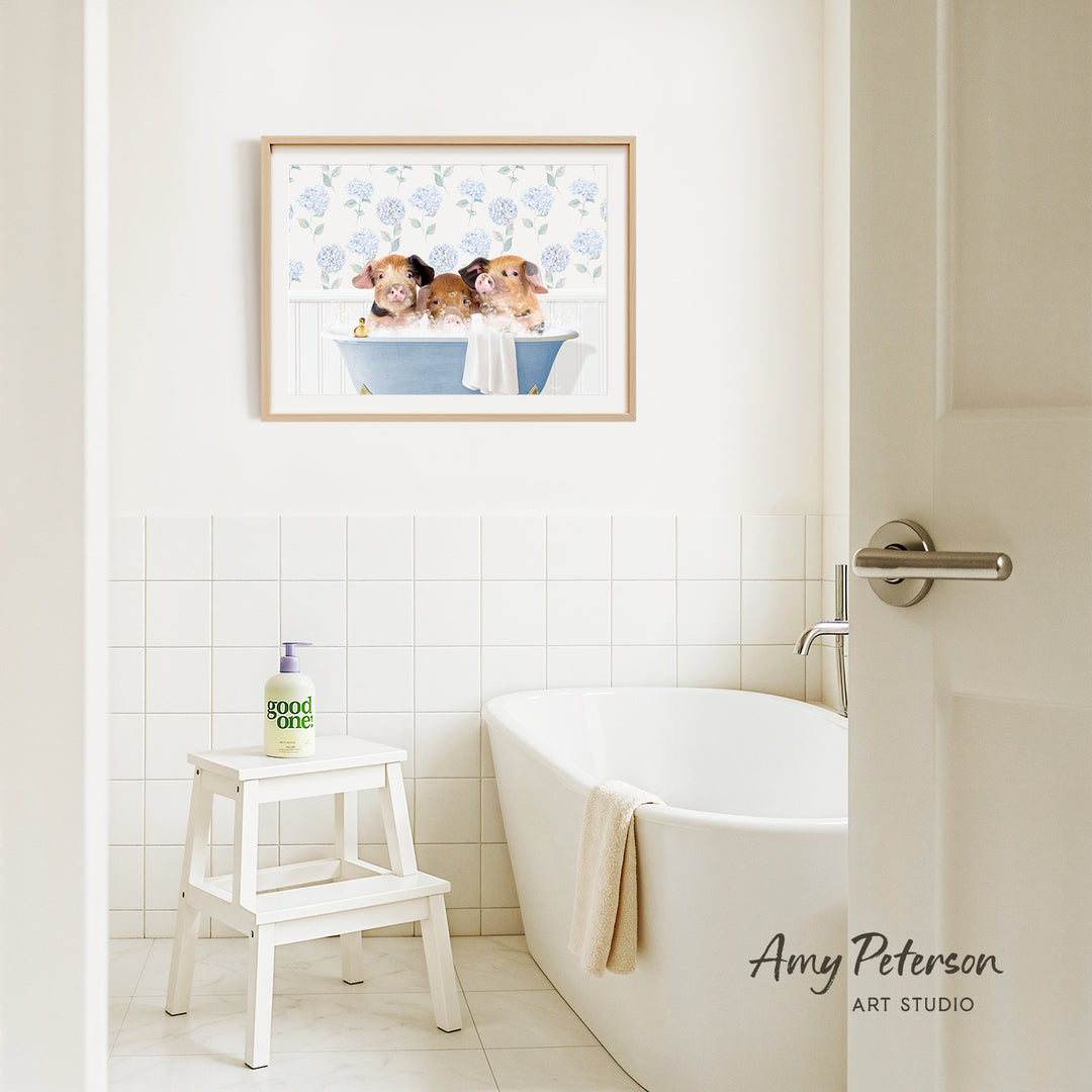 A framed image of three guinea pigs sitting in a bathtub is displayed on the wall above a white bathtub in a bathroom.