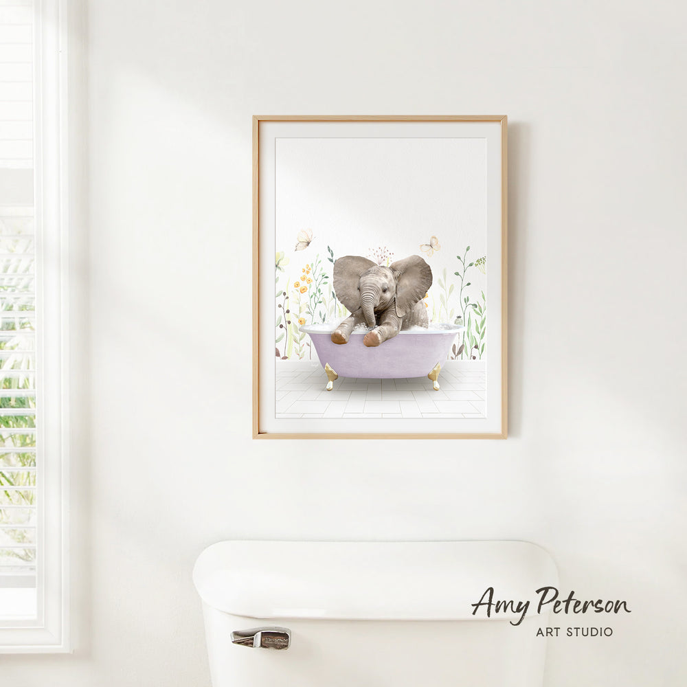 A framed illustration of an elephant sitting in a bathtub, surrounded by flowers and greenery, is hanging on a white wall.