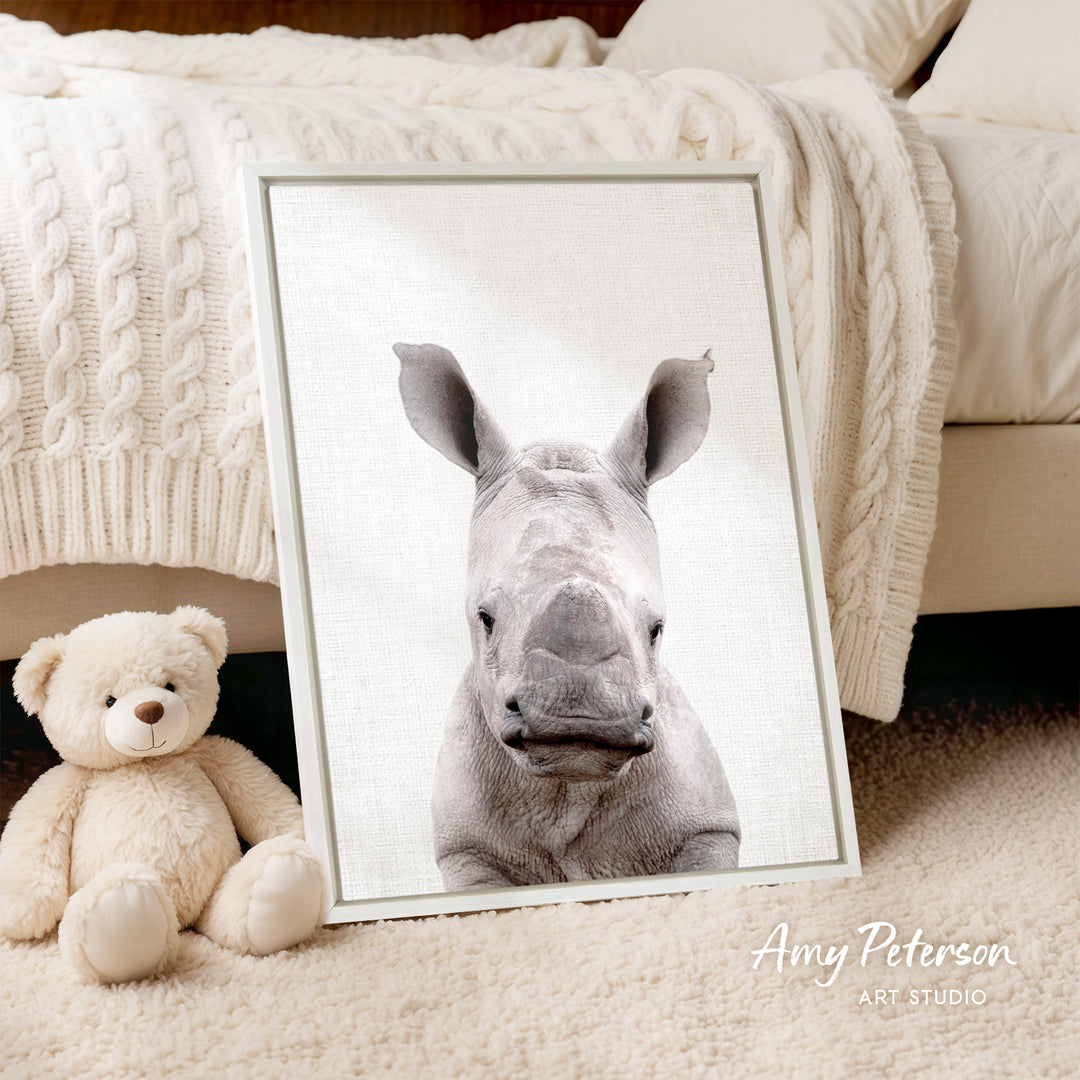 A framed photograph of a rhinoceros is displayed on a bed, accompanied by a teddy bear.