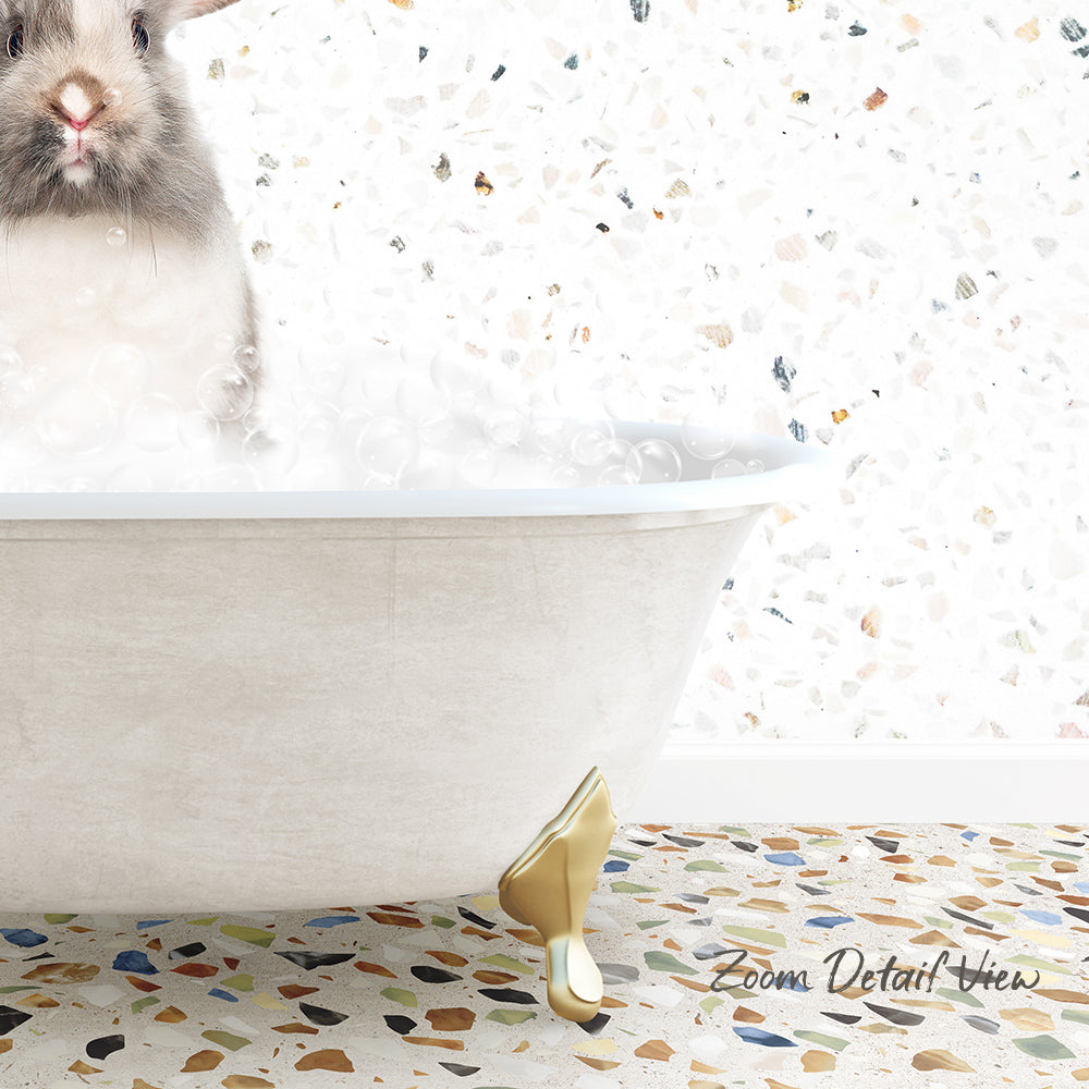 A fluffy white rabbit is sitting in a white bathtub filled with bubbles, with a mosaic tiled floor in the background.