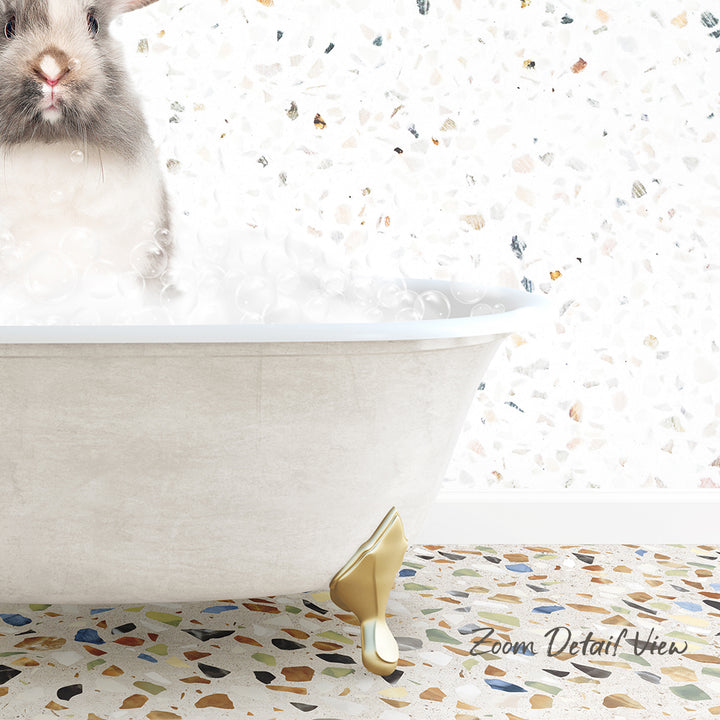 A fluffy white rabbit is sitting in a white bathtub filled with bubbles, with a mosaic tiled floor in the background.