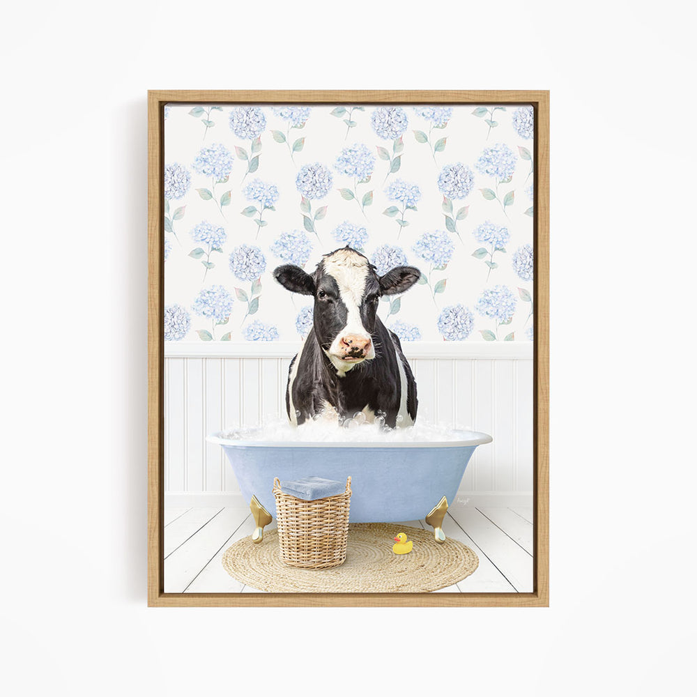A black and white cow is sitting in a blue bathtub filled with water, surrounded by a wicker basket and rubber ducks.
