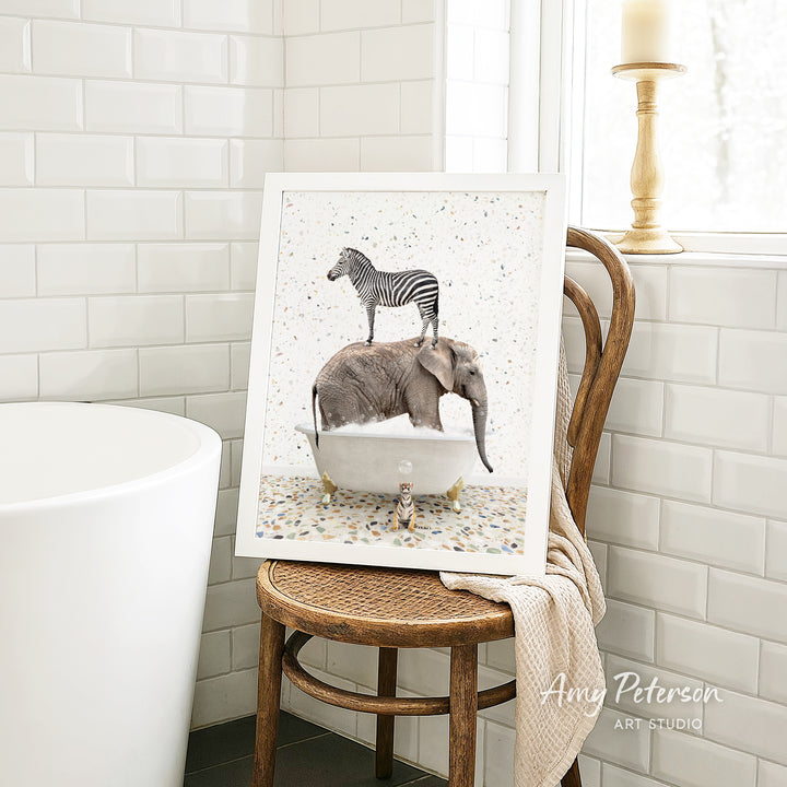 A framed image of a zebra standing on an elephant in a bathtub, with a towel draped over a chair in the background.