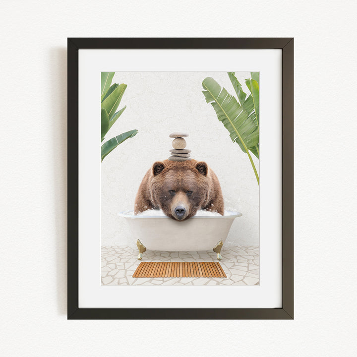 A brown bear is sitting in a white bathtub filled with water, surrounded by green plants and a wooden mat on the floor.