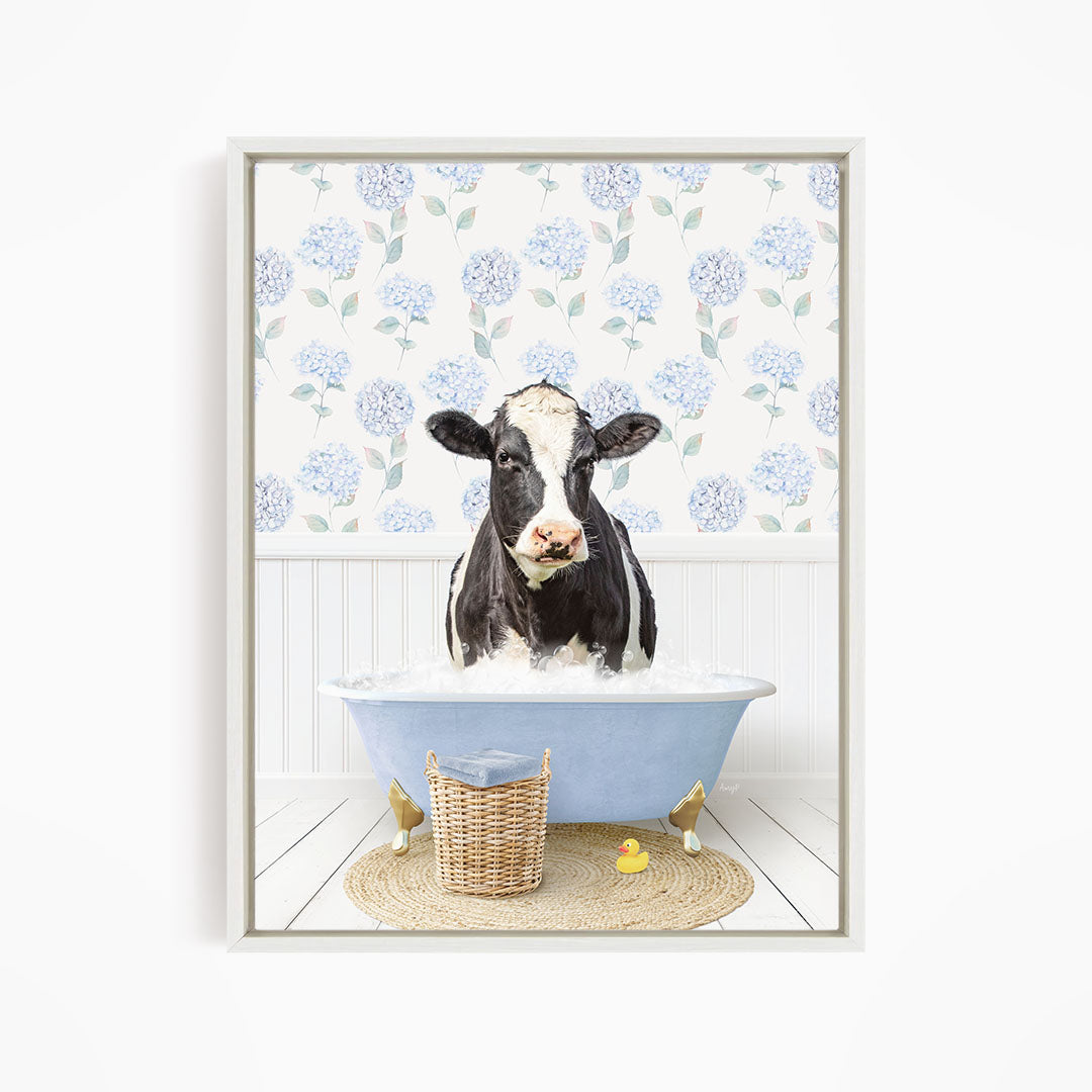 A black and white cow is sitting in a blue bathtub filled with water, surrounded by a wicker basket and a yellow rubber duck.