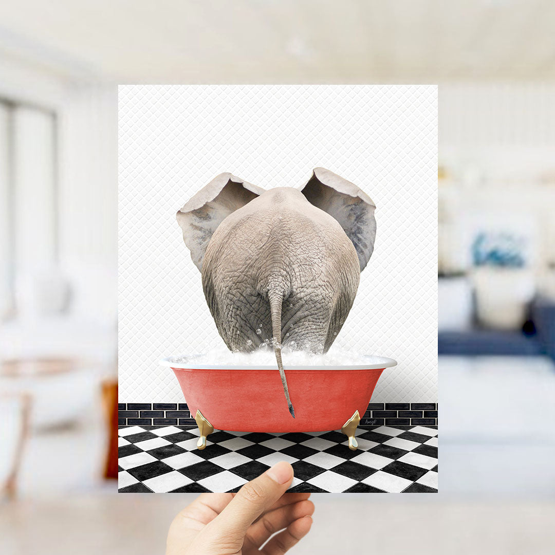 A hand holds up a framed image depicting an elephant sitting in a red bathtub filled with water, with a black and white checkered floor in the background.