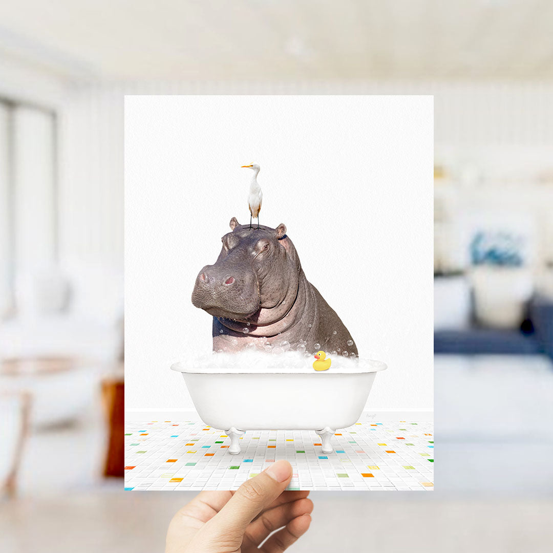 A hand holds up a framed image depicting a hippopotamus sitting in a bathtub, with a seagull perched on its head.