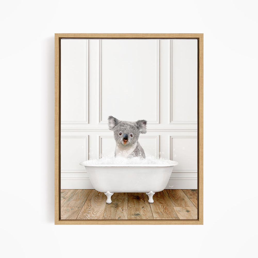 A koala bear sitting in a white bathtub filled with bubbles, looking directly at the camera.
