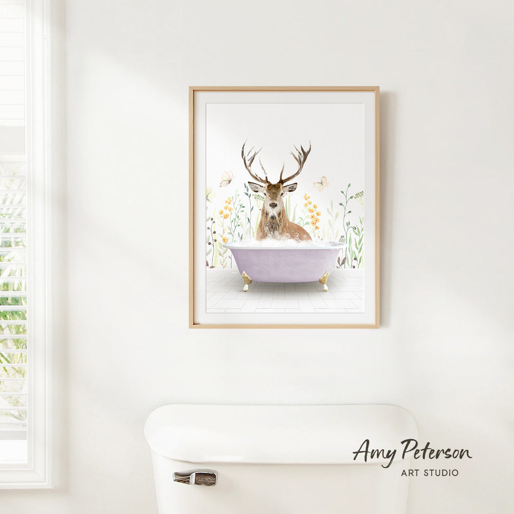 A framed print of a deer sitting in a bathtub is hanging on a white wall.